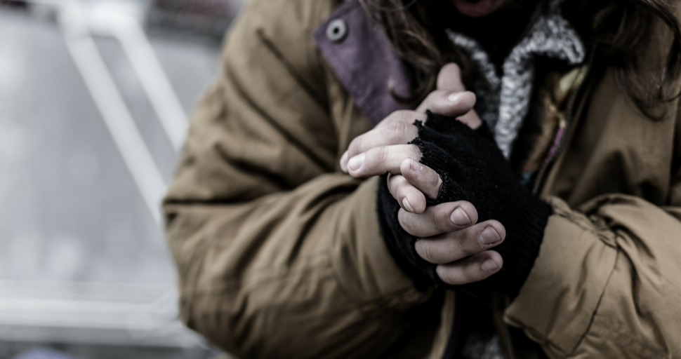 homeless person with fingerless gloves clasping their hands