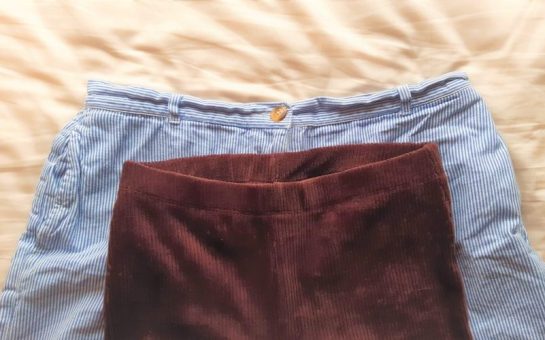 A pair of trousers with a small waistband lying on top of a pair of shorts with a larger waistband