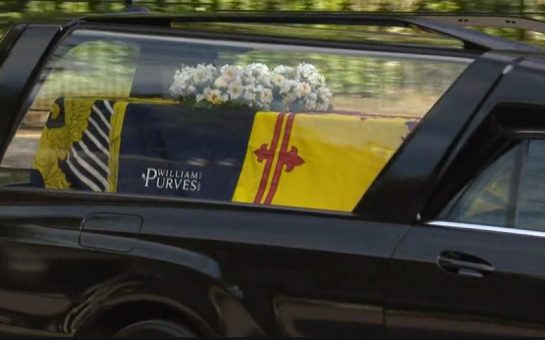 Queen Elizabeth's coffin wrapped in the Royal Standard of Scotland with a wreath of her favourite flowers from the Balmoral estate. Via iPlayer.