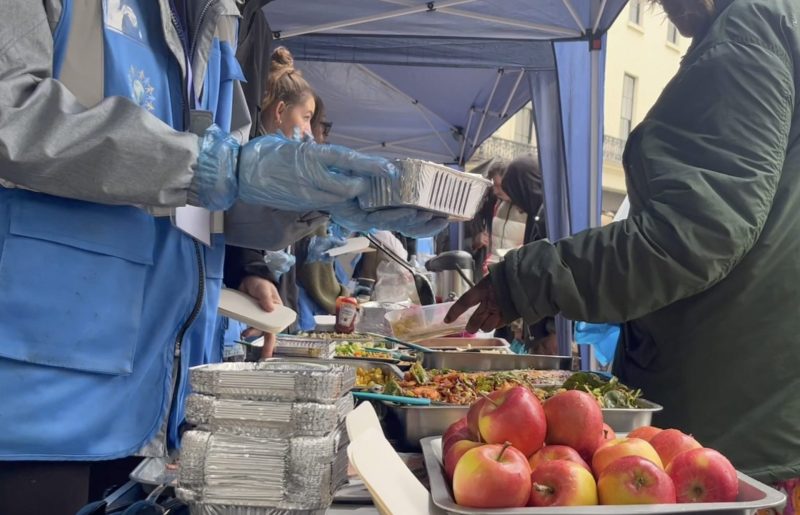 Volunteers from Refuge Network International serve food, including apples and salads, to the homeless and disadvantaged in silver containers