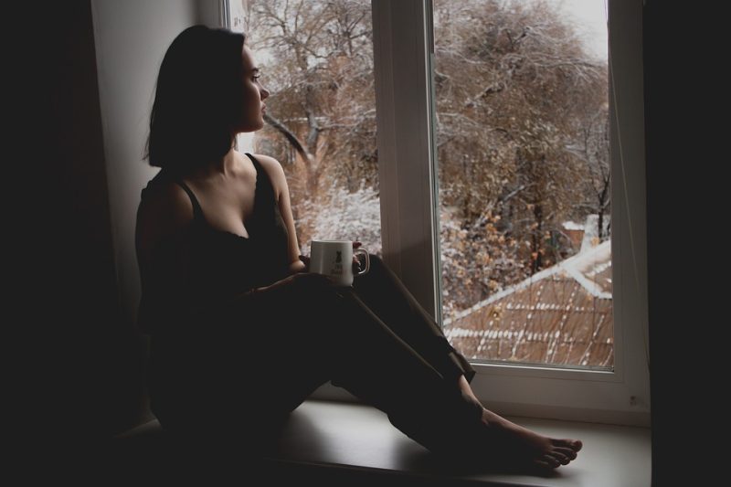 A woman sitting in a dark room looking out a window