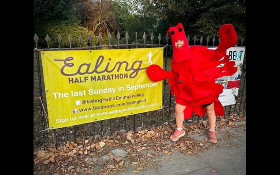 Woman dressed in lobster costume posing next to Half Marathon sign