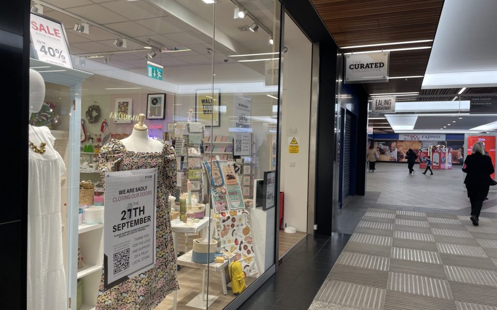 The exterior of the Store Collective in Ealing Broadway shopping centre. There are dresses and cards in the window and a closure sign.