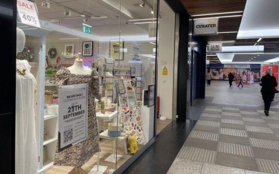 The exterior of the Store Collective in Ealing Broadway shopping centre. There are dresses and cards in the window and a closure sign.