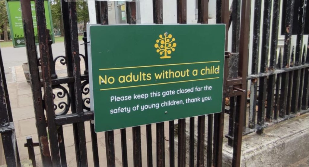A sign posted on the entrance to Coram's Fields reading "No adults without a child. Please keep this gate closed for the safety of young children, thank you."