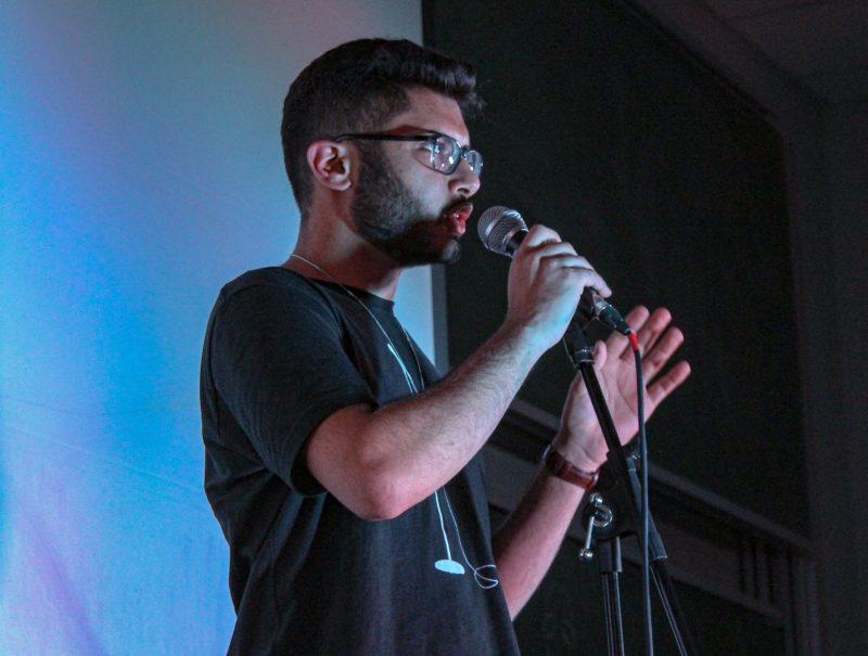 Rohan Ashar speaking into a microphone, performing at comedy show