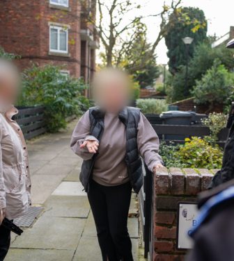 Members of the public with blurred out faces speak to the police in a built-up housing estate.