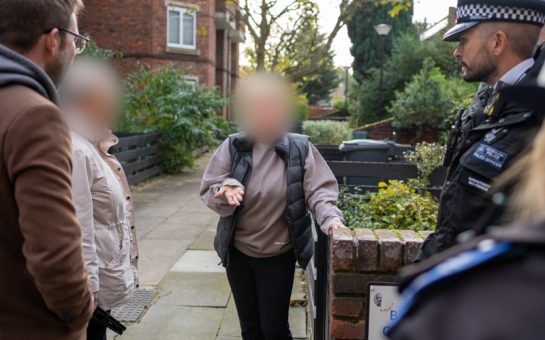 Members of the public with blurred out faces speak to the police in a built-up housing estate.