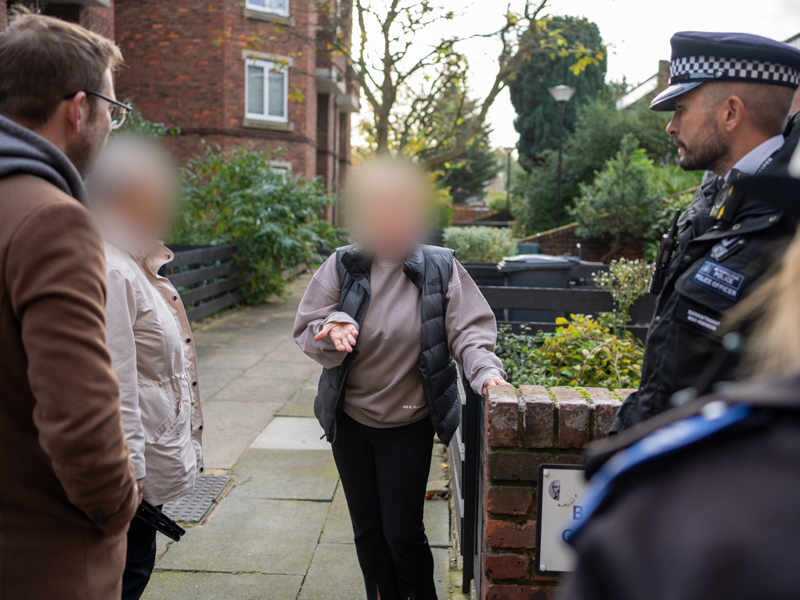 Members of the public with blurred out faces speak to the police in a built-up housing estate.