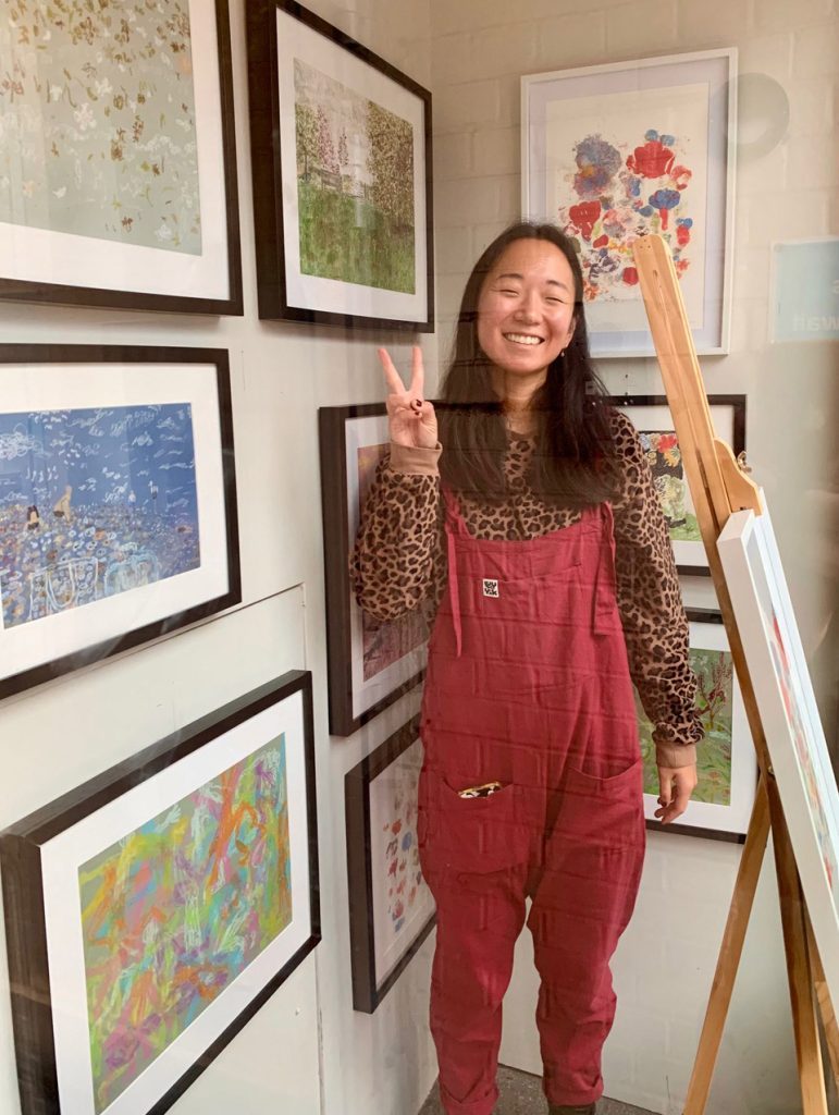 An image of Jolene Liam in front of her art in the display window. Picture was taken by JJ Campbell, founder of SpringUp Art Gallery