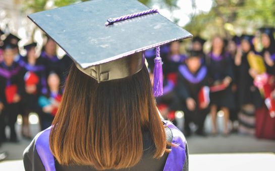 Image shows someone in a graduation cap and gown facing away from the camera.