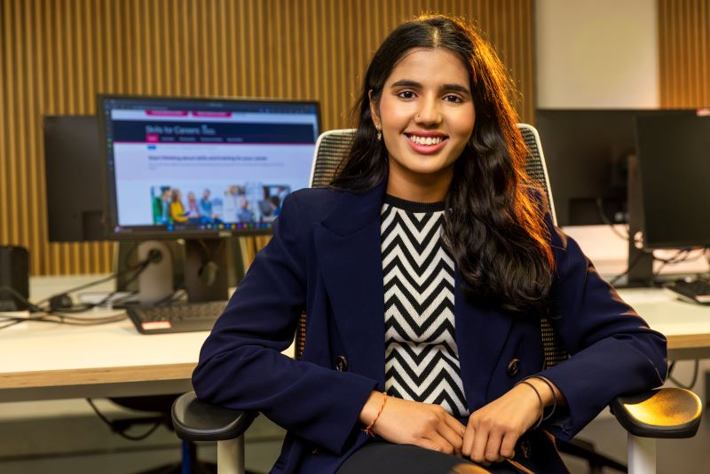 Photo of Krisha Dhanasekaran sitting on a chair and smiling at the camera