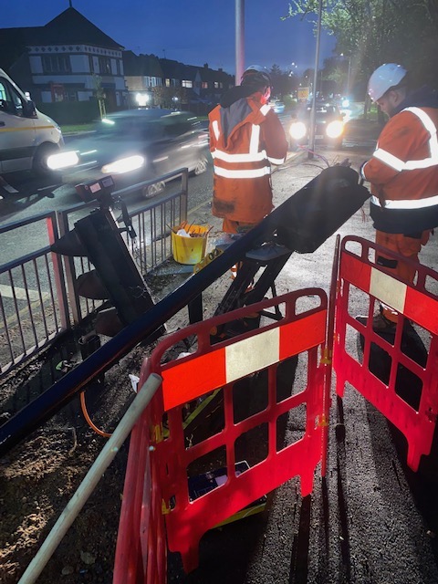 Picture showing ULEZ camera cut in half while workers in orange high-vis fix it.