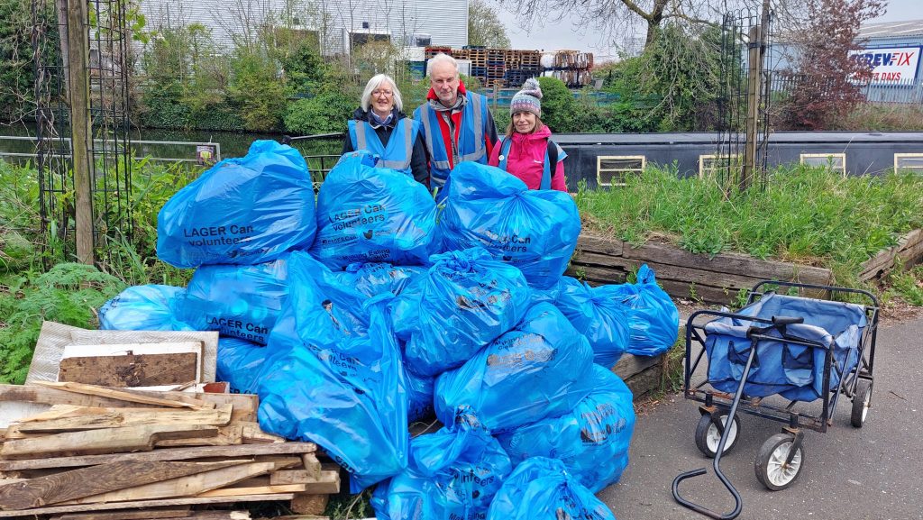 Three volunteers standing behind a mountain of rubbish sacks filled with rubbish.