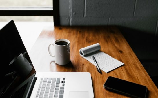 A photo of a computer, notepad and phone on a desk