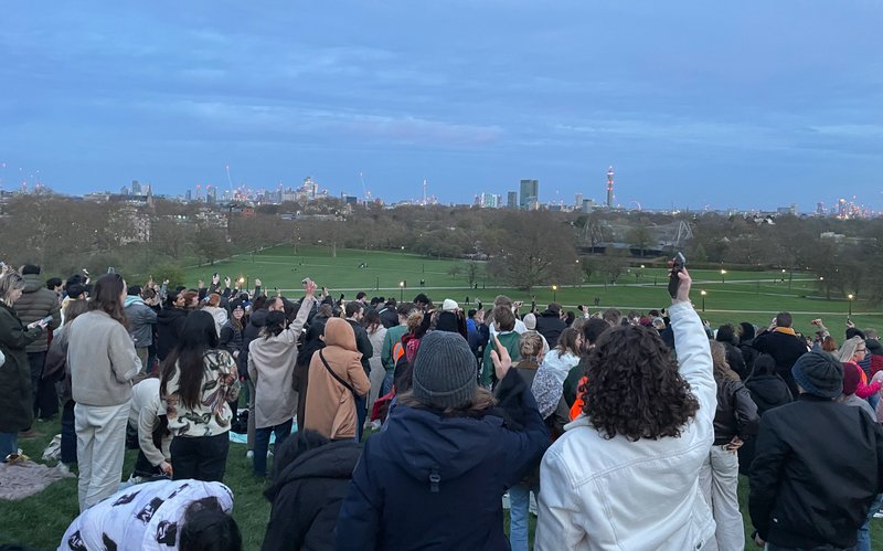 Crowd of people hold their phones above them, facing away from camera down Primrose Hill.