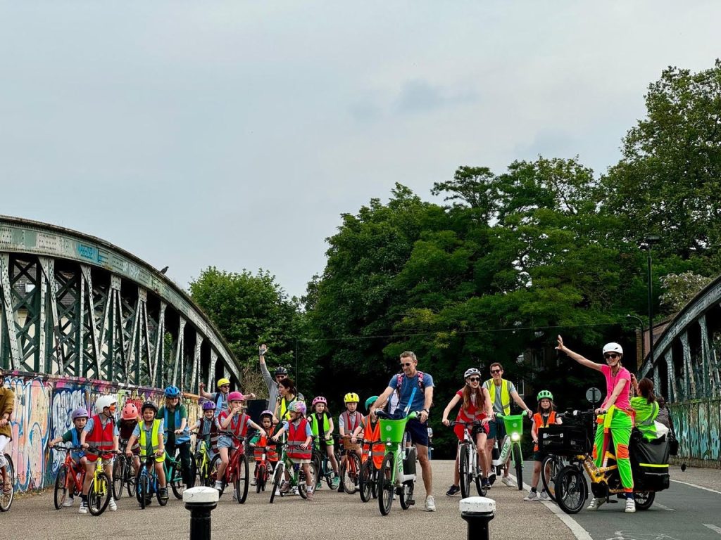 A group of children and adults all in high visibility jackets cycling along a bridge.