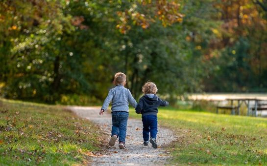 Two young boys holding hands and running through a green space.