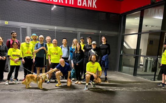 An Achilles UK group photo, several members wearing fluorescent yellow shirts with running gear by Emirates Stadium.