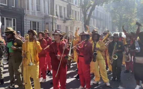 Attendees dancing down the street at Notting Hill Carnival, with bright yellow and red outfits.