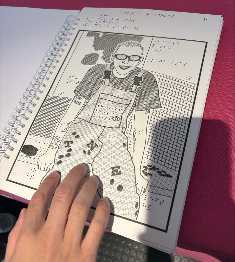 A tactile book, the book is opened to an image of a smiling man sitting down wearing dungarees, the picture is made up of braille and there is a hand feeling the image.