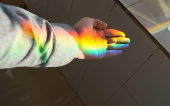 Child's hand catching rainbow light ray from window