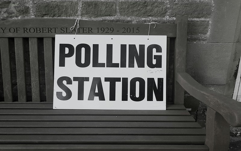 A picture of a sign saying "Polling Station" tied to a wooden bench. Photo by Steve Houghton-Burnett on Unsplash