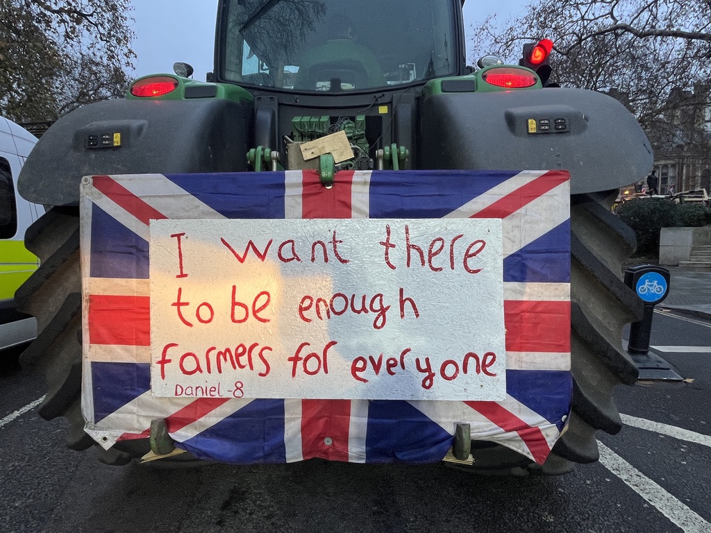 A close up of a tractor with a placard with Union Jack and text saying "I want there to be enough farmers for everyone. Daniel - 8".
