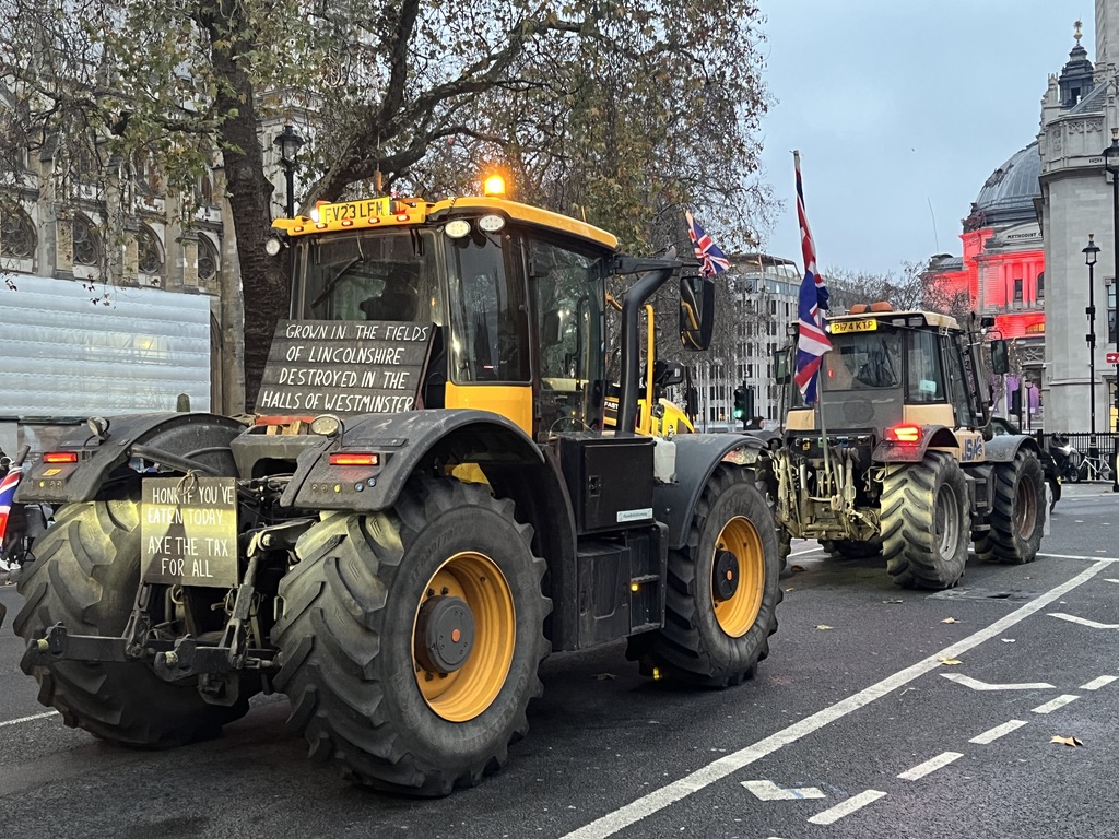 A yellow tractor with placards reading "Grown in the fields of Lincolnshire, destroyed in the halls of Westminster" and "honk if you've eaten today. Axe the tax for all".