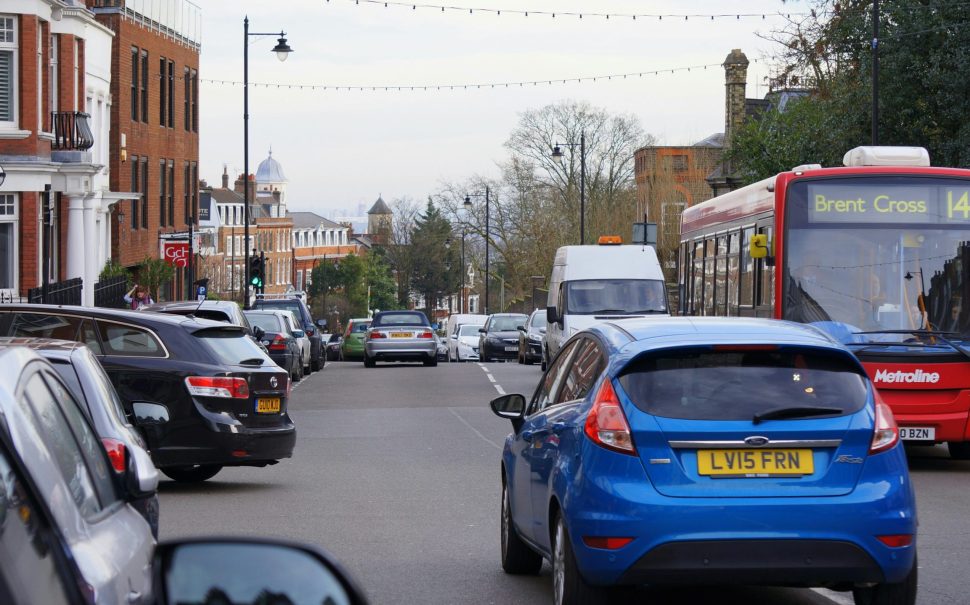 A busy street in Brent with lots of cars, a blue Ford Focus in the foreground and a red bus heading to Brent Cross on the right hand side.