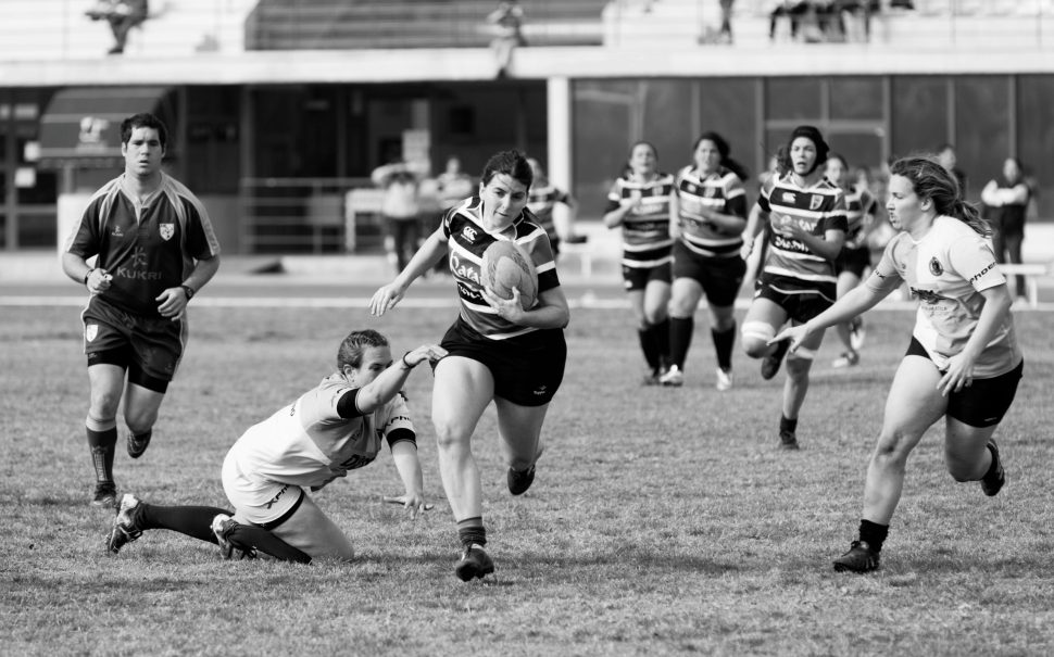 The photograph is of female rugby players. One lady attempting to tackle another while she is running with the ball.
