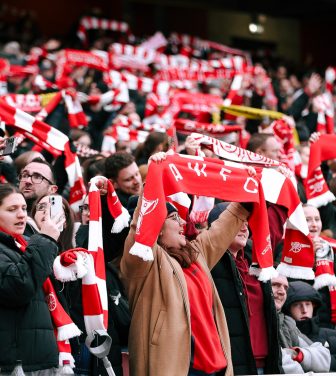 Arsenal fans in the Emirates Stadium stands holding their scarves up supporting their team (Credit: Suzy Lycett)