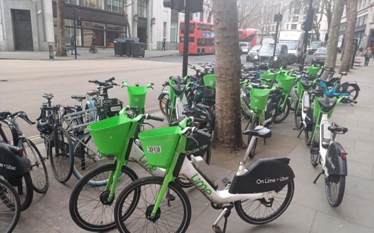 Dozens of Lime bikes parked alongside private bikes on a London street.