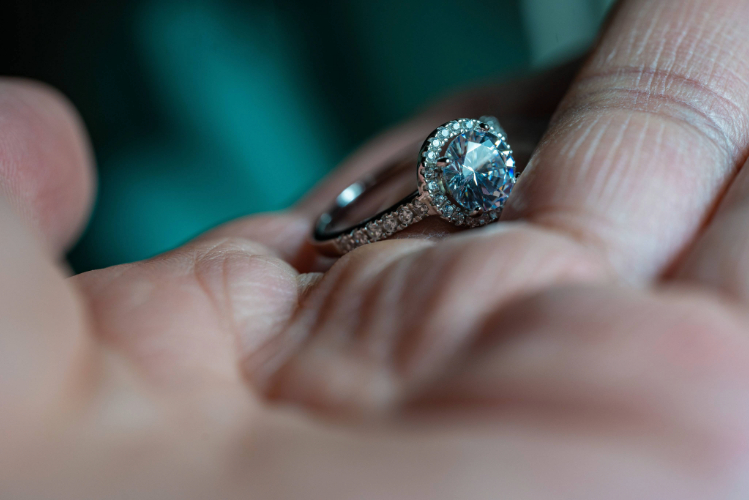 A person's hand holding a diamond ring.