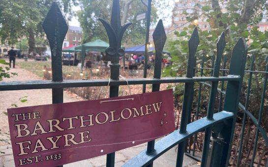 A banner for the Bartholomew Fayre attached to a gate in front of the fair.