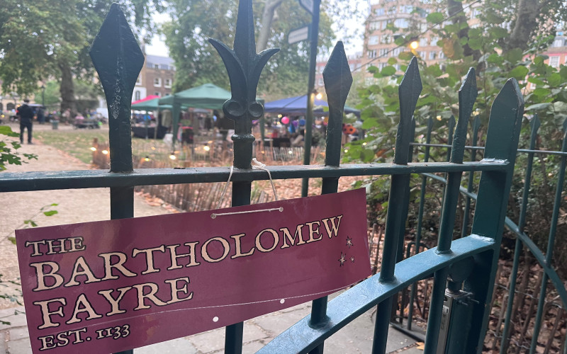 A banner for the Bartholomew Fayre attached to a gate in front of the fair.