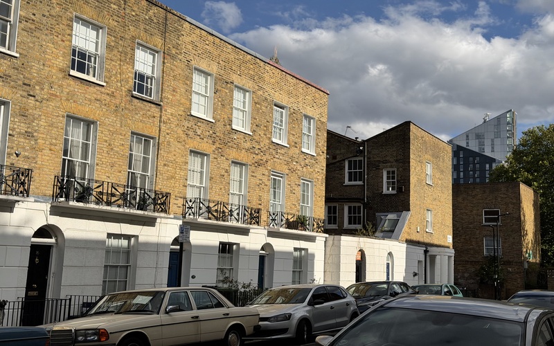 Brick townhouses on a road in Somers Town, London, with parked cars and a modern building in the background.